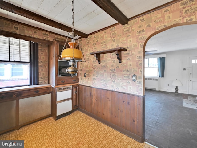 kitchen featuring arched walkways, beam ceiling, a wainscoted wall, radiator, and hanging light fixtures