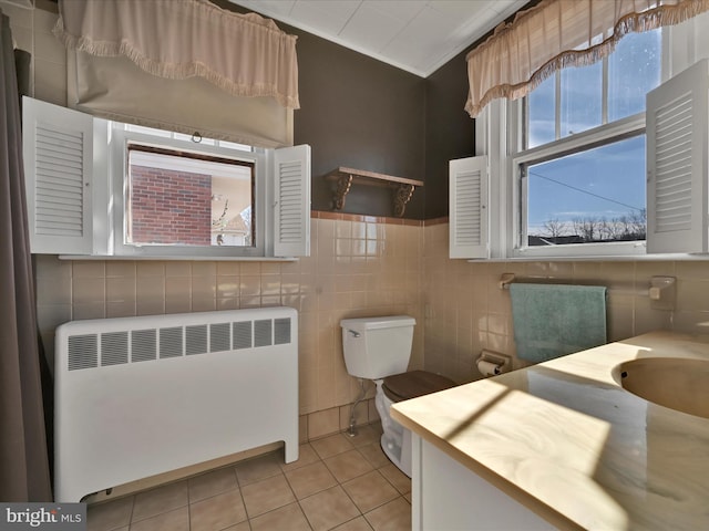 bathroom featuring toilet, radiator heating unit, tile patterned flooring, vanity, and tile walls