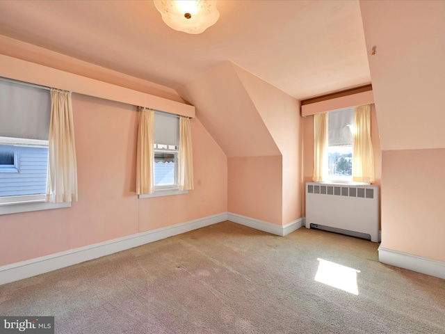 additional living space with radiator, baseboards, vaulted ceiling, and light colored carpet