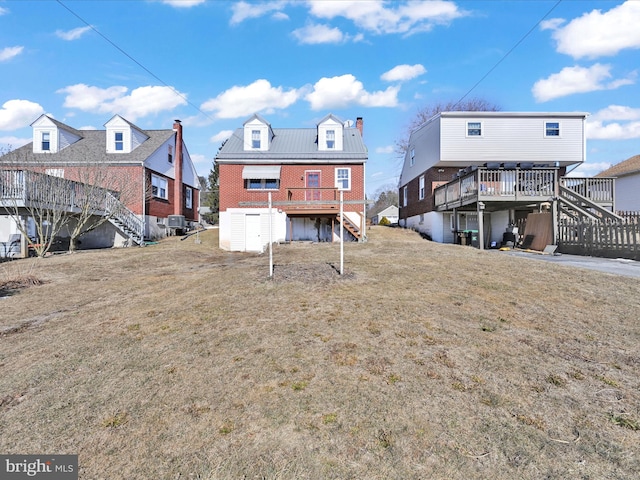 rear view of house with a deck, brick siding, a yard, and stairway