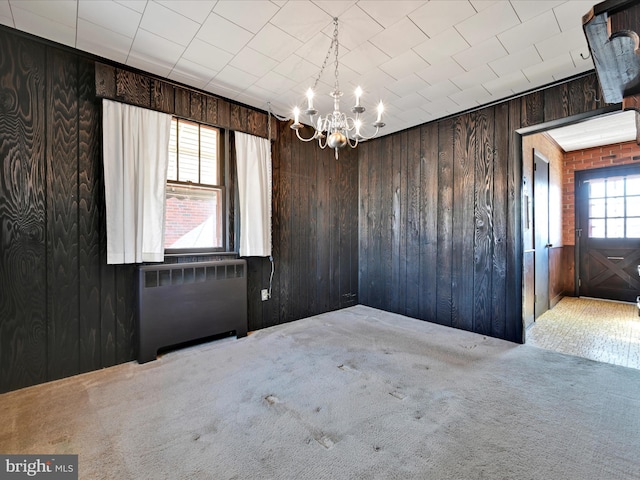 unfurnished room with carpet floors, radiator, a notable chandelier, and wooden walls