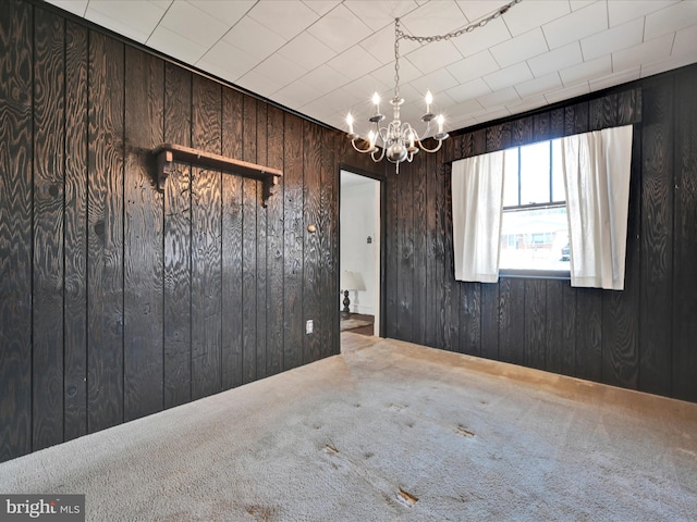 spare room featuring wooden walls, carpet floors, and a notable chandelier