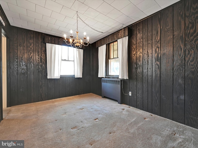 spare room with radiator, wood walls, light carpet, and a notable chandelier