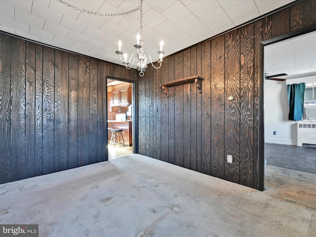 carpeted empty room featuring radiator, wood walls, and an inviting chandelier