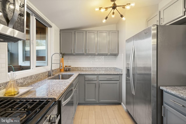 kitchen featuring lofted ceiling, a sink, appliances with stainless steel finishes, gray cabinets, and decorative backsplash