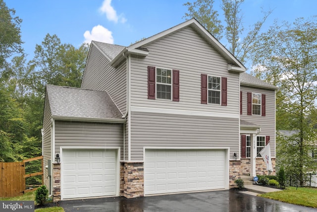 traditional home with driveway, stone siding, fence, and roof with shingles