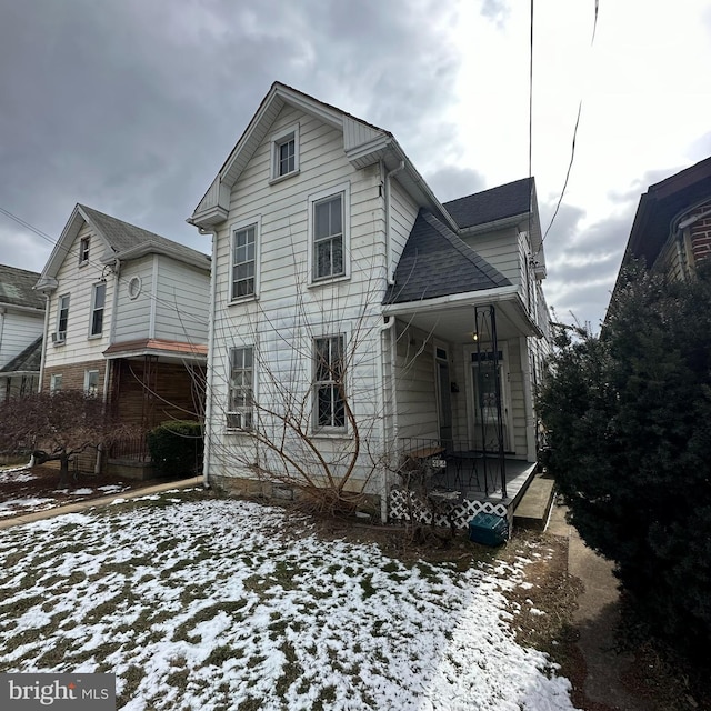 snow covered back of property featuring a shingled roof