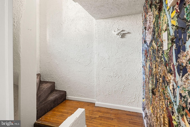 interior details featuring a textured ceiling, a textured wall, wood finished floors, and baseboards