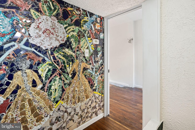 interior space featuring a textured ceiling, a textured wall, wood-type flooring, and baseboards