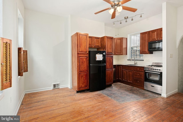 kitchen with visible vents, hardwood / wood-style flooring, light countertops, black appliances, and a sink