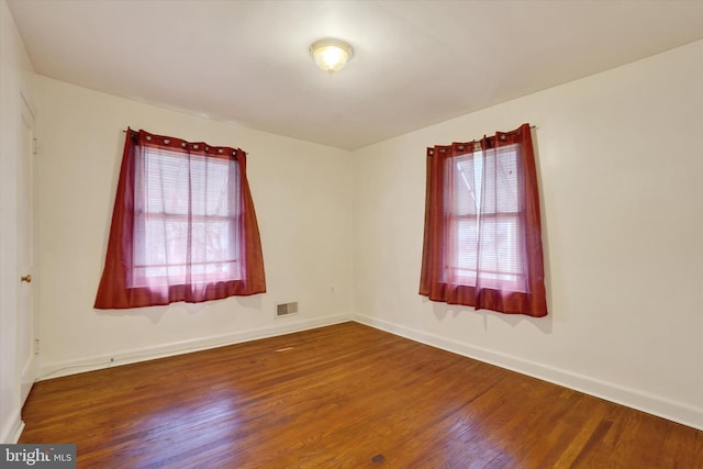 unfurnished room featuring baseboards, visible vents, and wood finished floors