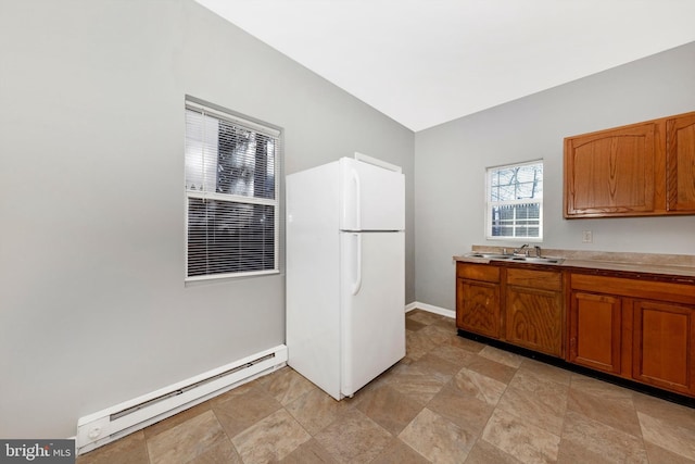 kitchen with brown cabinets, light countertops, baseboard heating, freestanding refrigerator, and a sink