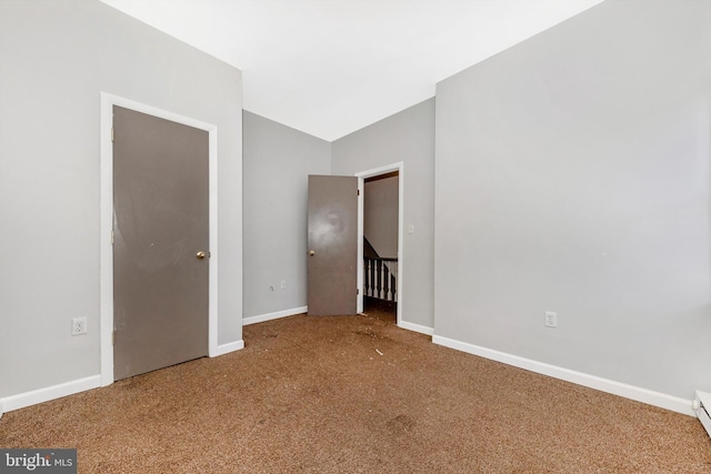 carpeted empty room featuring vaulted ceiling, a baseboard radiator, and baseboards