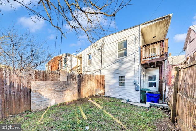 back of house featuring a fenced backyard, a lawn, and a balcony