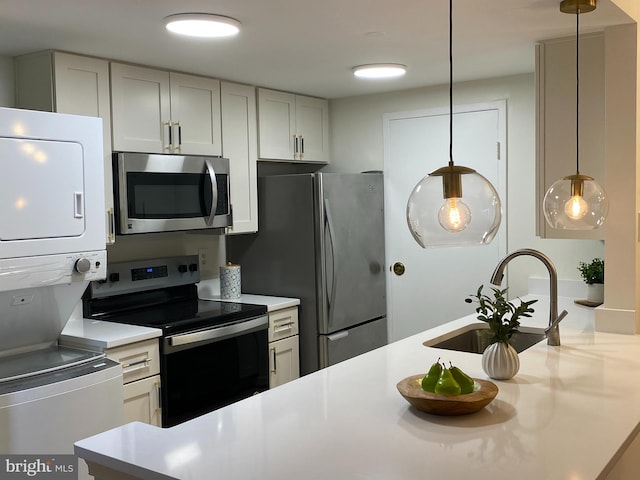 kitchen with pendant lighting, stainless steel appliances, light countertops, and stacked washer / drying machine