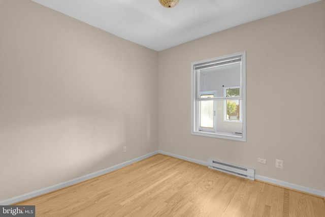 spare room with a baseboard heating unit, light wood-type flooring, and baseboards