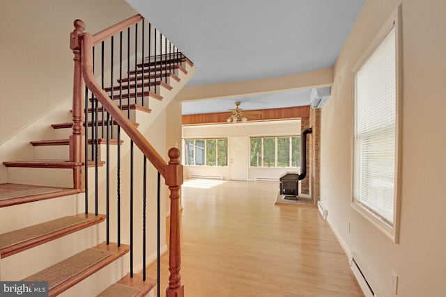 staircase with a baseboard heating unit, a wall mounted air conditioner, wood finished floors, and baseboards