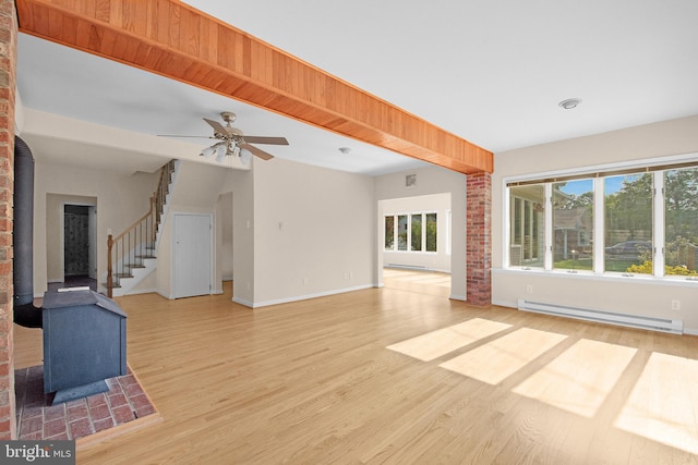 unfurnished living room featuring a baseboard heating unit, a wealth of natural light, a wood stove, and stairs