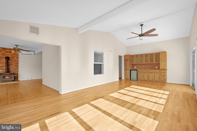 unfurnished living room featuring light wood finished floors, visible vents, lofted ceiling with beams, a ceiling fan, and a wood stove