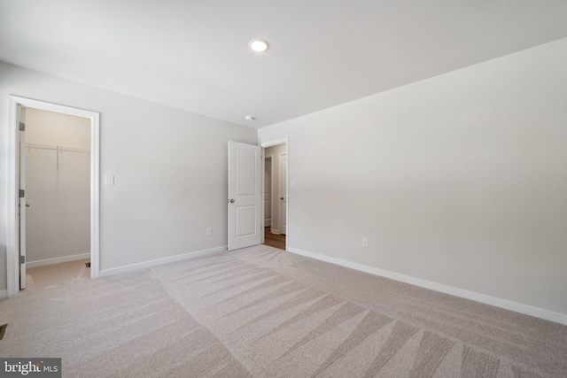 unfurnished bedroom with recessed lighting, baseboards, a walk in closet, and light colored carpet