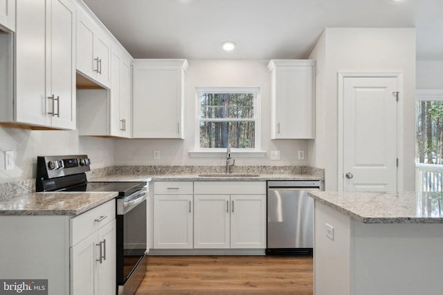 kitchen featuring light stone counters, stainless steel appliances, light wood-style flooring, white cabinetry, and a sink