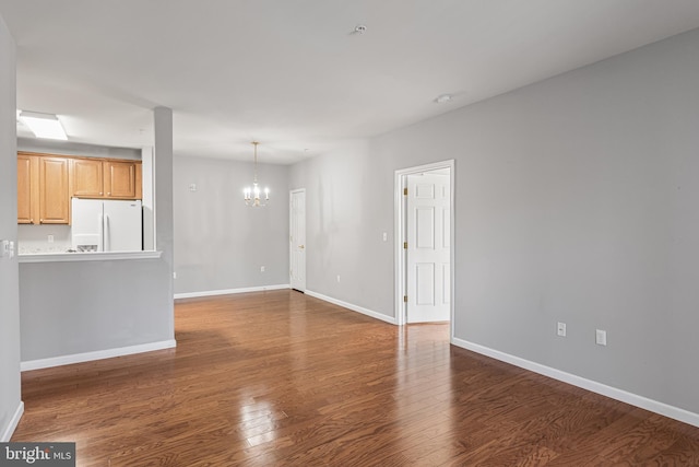 unfurnished living room featuring dark wood-type flooring, baseboards, and an inviting chandelier