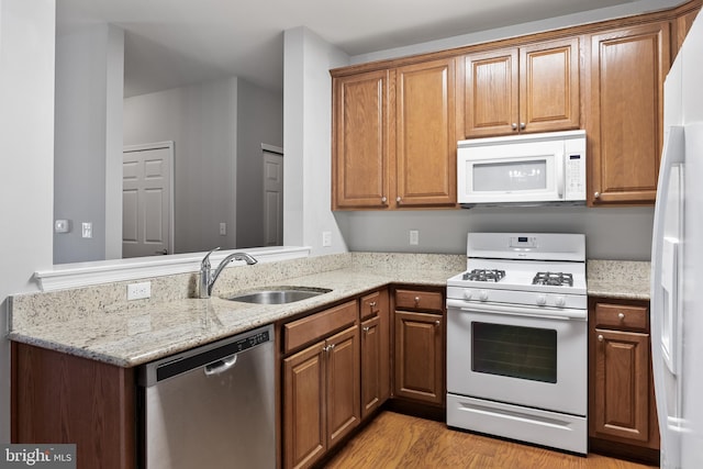 kitchen featuring light wood-type flooring, white appliances, brown cabinets, and a sink