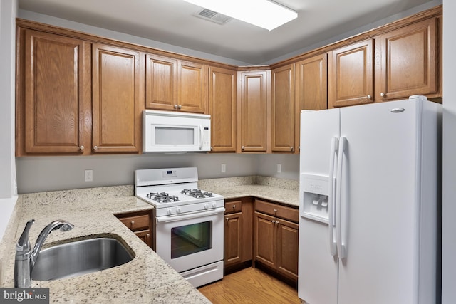 kitchen featuring light stone counters, white appliances, a sink, brown cabinets, and light wood finished floors