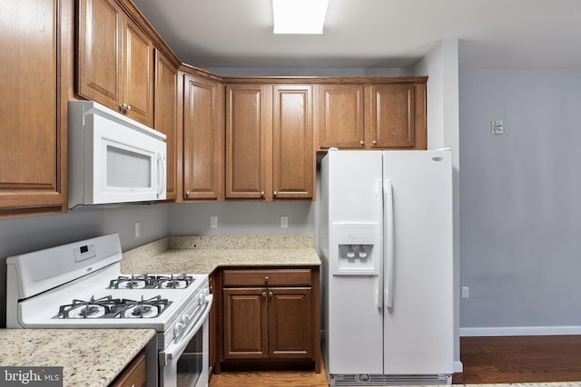 kitchen with white appliances, baseboards, brown cabinetry, wood finished floors, and light stone countertops