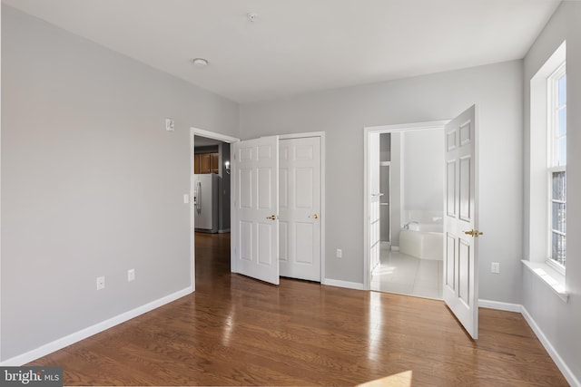 unfurnished bedroom with connected bathroom, white refrigerator with ice dispenser, wood finished floors, baseboards, and a closet