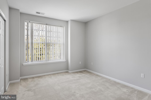 spare room with light carpet, visible vents, and baseboards