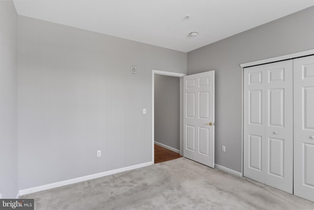 unfurnished bedroom with a closet, light carpet, and baseboards