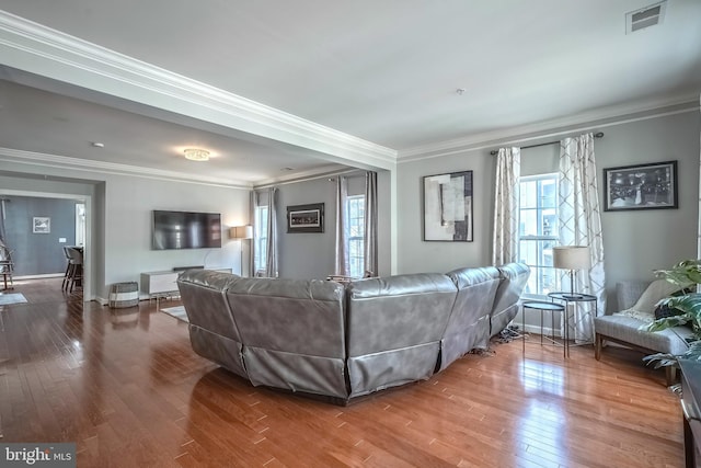 living room with baseboards, wood finished floors, visible vents, and crown molding