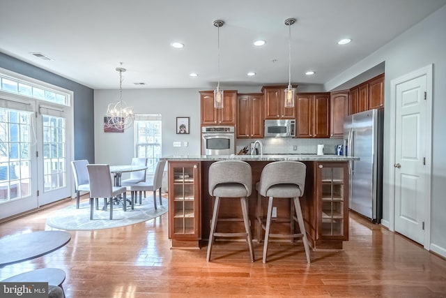 kitchen with light stone counters, stainless steel appliances, visible vents, hanging light fixtures, and an island with sink