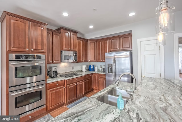 kitchen featuring decorative backsplash, light stone counters, appliances with stainless steel finishes, decorative light fixtures, and a sink