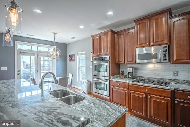 kitchen featuring hanging light fixtures, light stone countertops, appliances with stainless steel finishes, and a sink