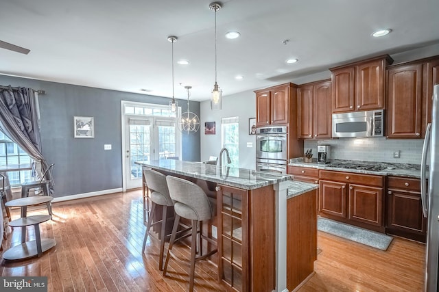 kitchen with light stone countertops, a kitchen island with sink, appliances with stainless steel finishes, and decorative light fixtures