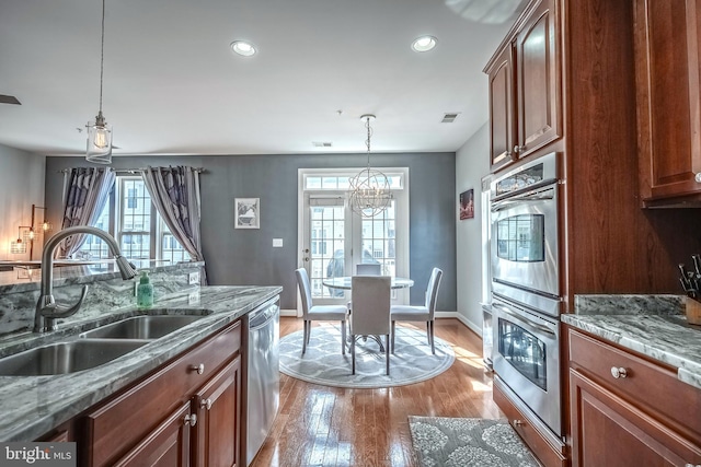 kitchen featuring stainless steel appliances, a sink, visible vents, light stone countertops, and decorative light fixtures