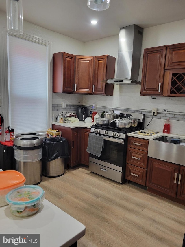 kitchen with stainless steel gas range oven, light wood-style floors, light countertops, backsplash, and wall chimney exhaust hood