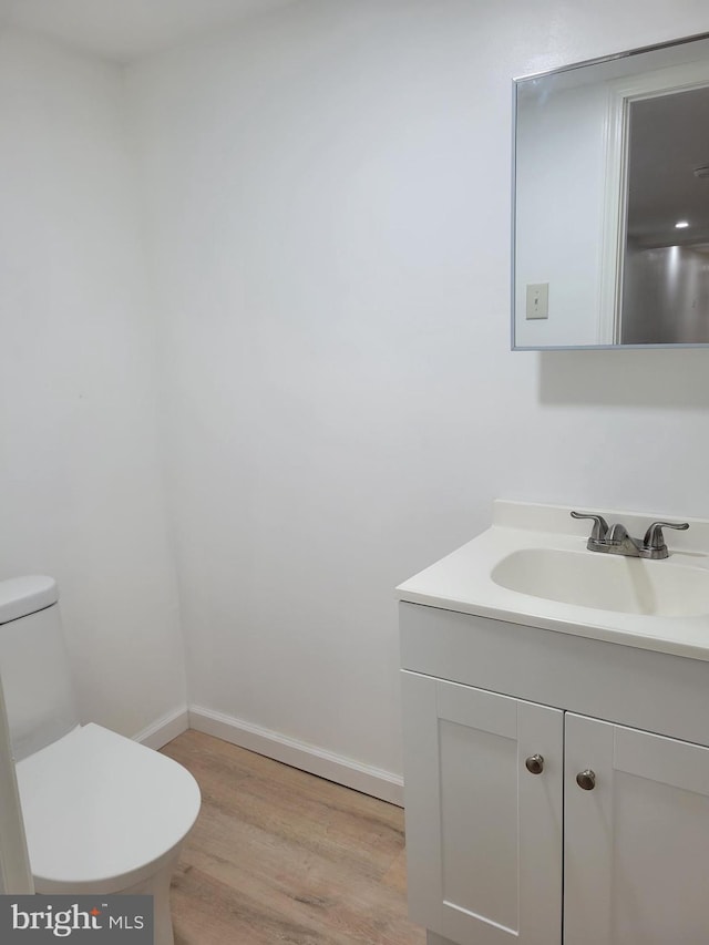 half bathroom with toilet, baseboards, wood finished floors, and vanity