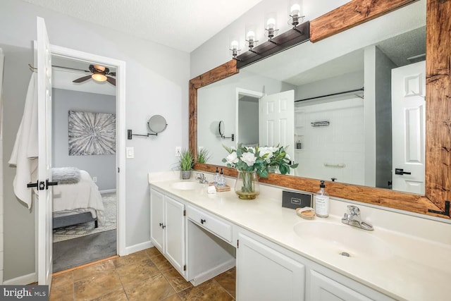 ensuite bathroom with ceiling fan, a textured ceiling, double vanity, a shower, and baseboards