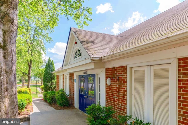 property entrance featuring brick siding, french doors, and a shingled roof
