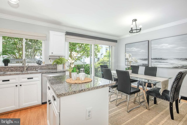 kitchen featuring stainless steel dishwasher, white cabinetry, a sink, light stone countertops, and crown molding
