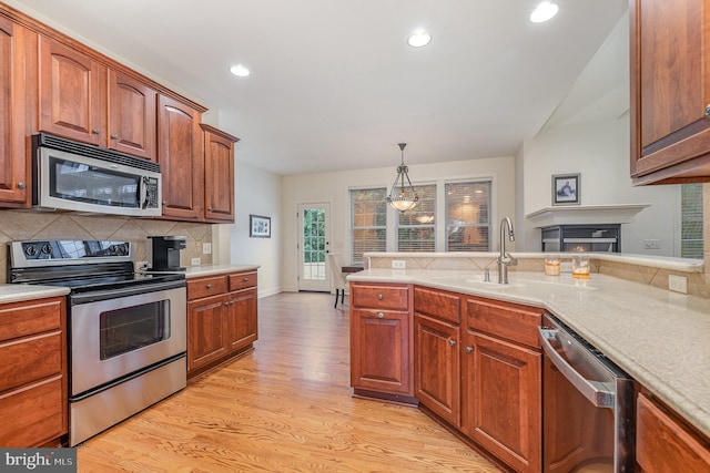 kitchen featuring appliances with stainless steel finishes, backsplash, brown cabinets, light wood finished floors, and pendant lighting