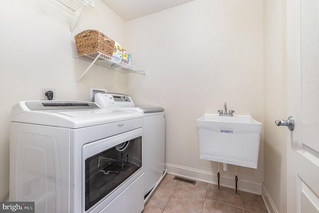 washroom featuring laundry area, light tile patterned floors, baseboards, washer and dryer, and a sink