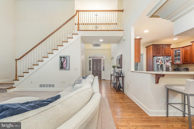 living area with recessed lighting, a towering ceiling, visible vents, baseboards, and light wood finished floors