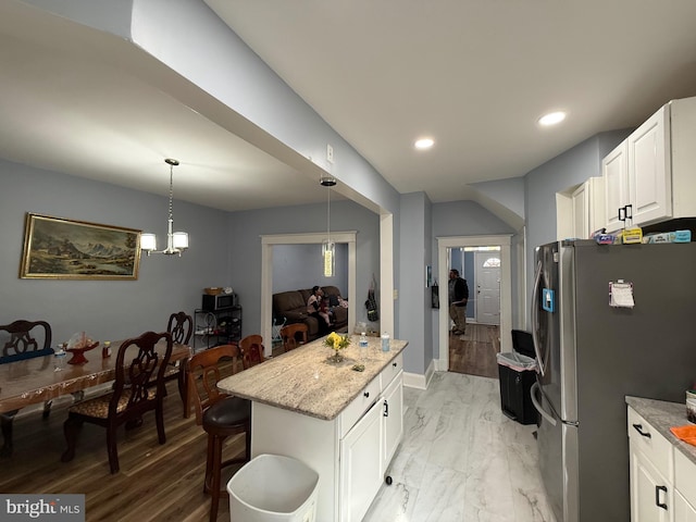 kitchen with a center island, hanging light fixtures, freestanding refrigerator, a kitchen bar, and white cabinetry