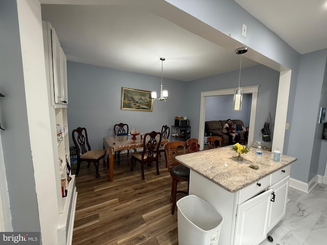 kitchen with pendant lighting, a breakfast bar area, white cabinetry, light stone countertops, and baseboards