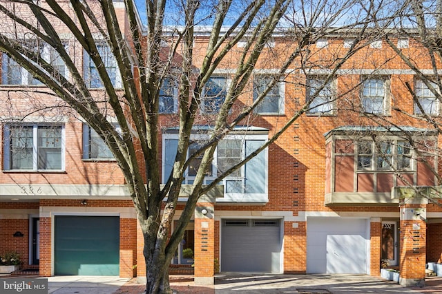 multi unit property featuring a garage, driveway, and brick siding