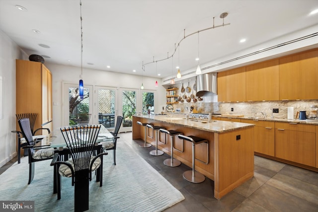 kitchen with hanging light fixtures, tasteful backsplash, a center island with sink, and extractor fan